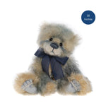 A small plush teddy bear with fluffy gray and beige fur, a dark blue ribbon bow, and gray paws, shown on a white background with a blue circular badge that reads '16 Inches'.